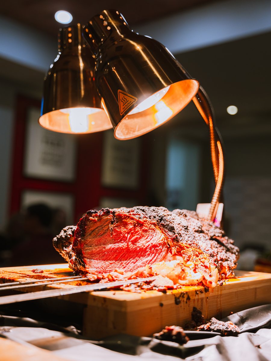 A carving station of slow-roasted beef under warming lamps at a ChefsPrep Catering event