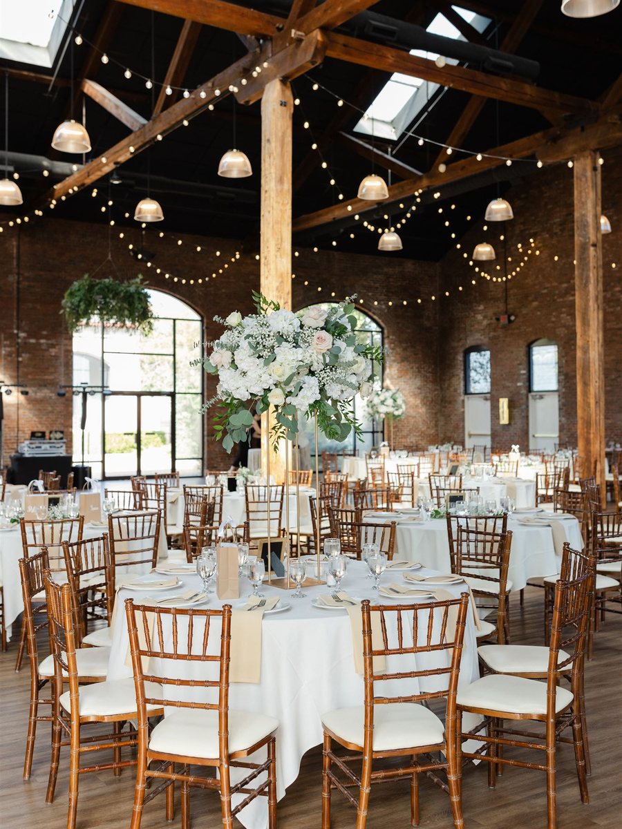 A wedding reception set with gold chairs, white florals, and string lights, catered by ChefsPrep Catering